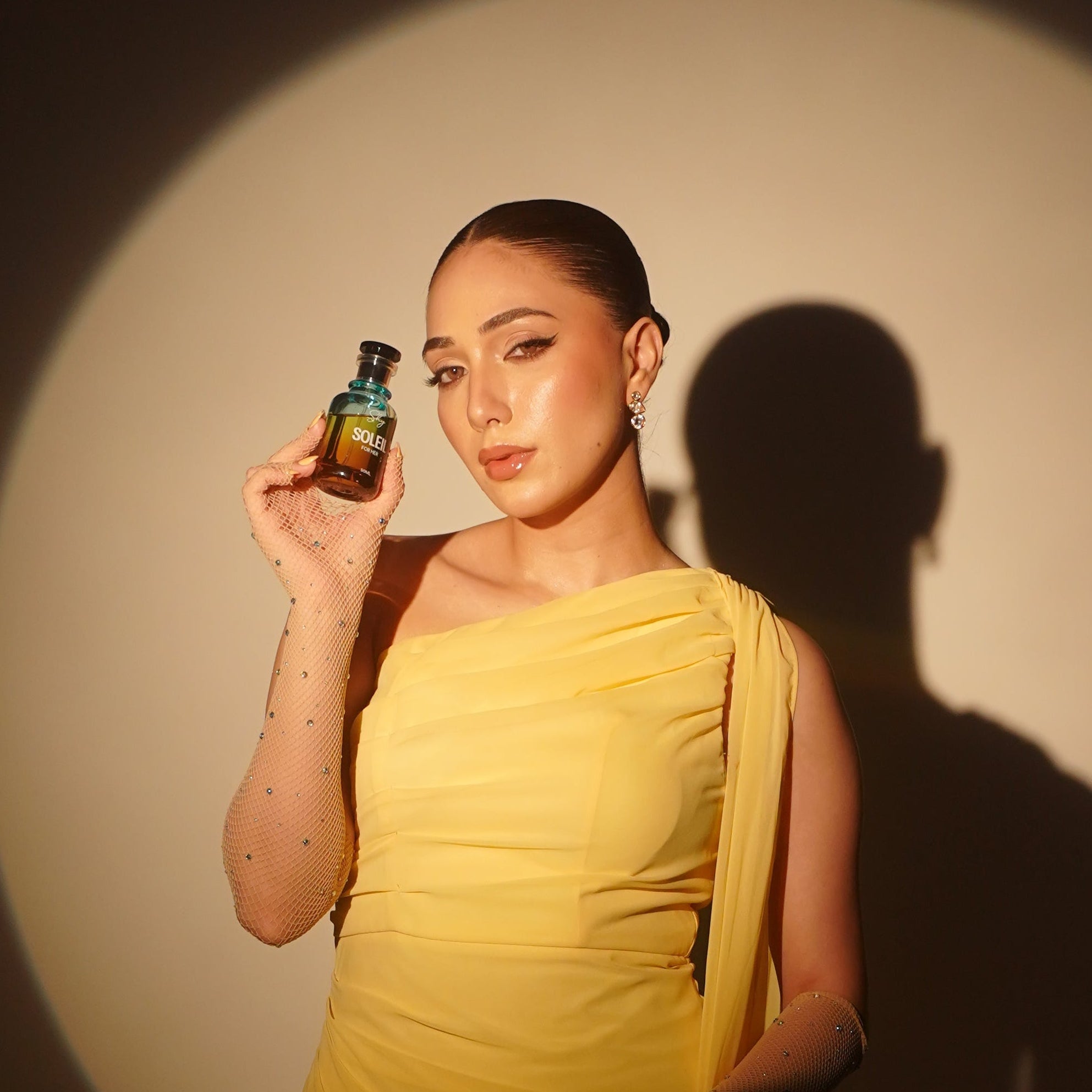 Woman in a yellow dress holding a small bottle against a dark background with a spotlight effect.
